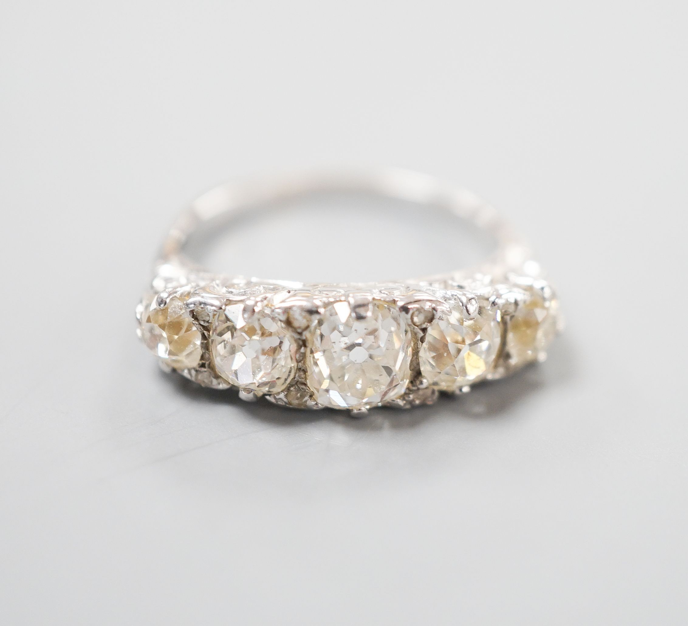 A white metal and graduated five stone old cut diamond set half hoop ring, with diamond chip spacers, size L, gross weight 3.7 grams.